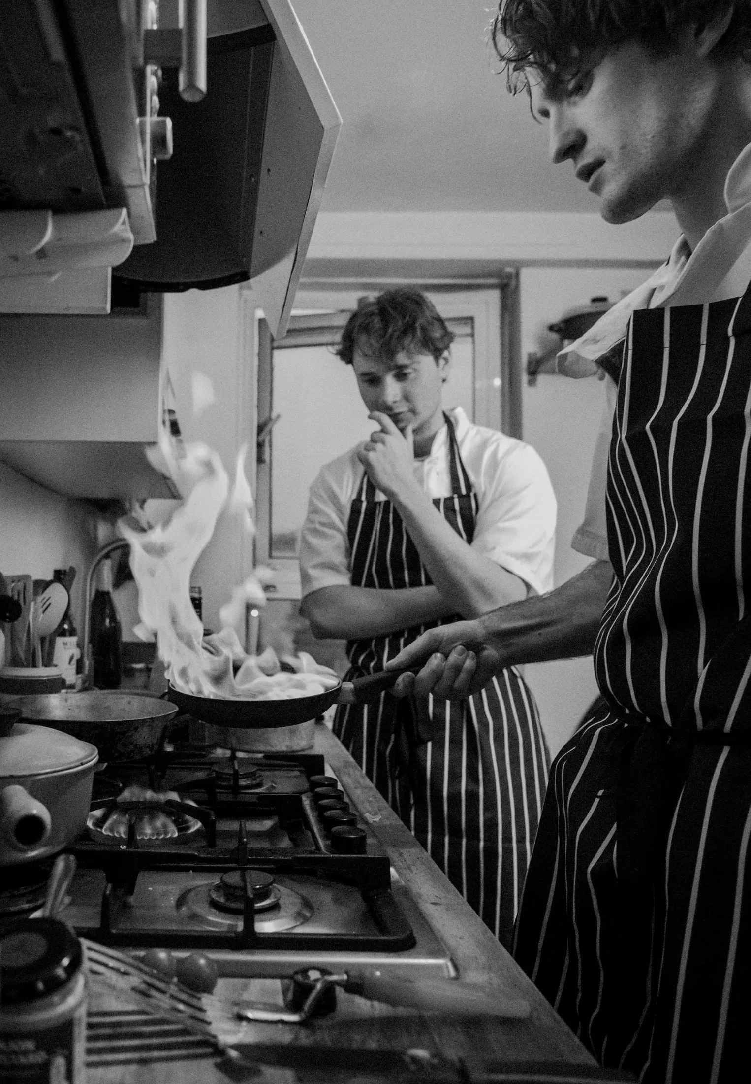 A chef in whites leans both arms on a stainless-steel counter.