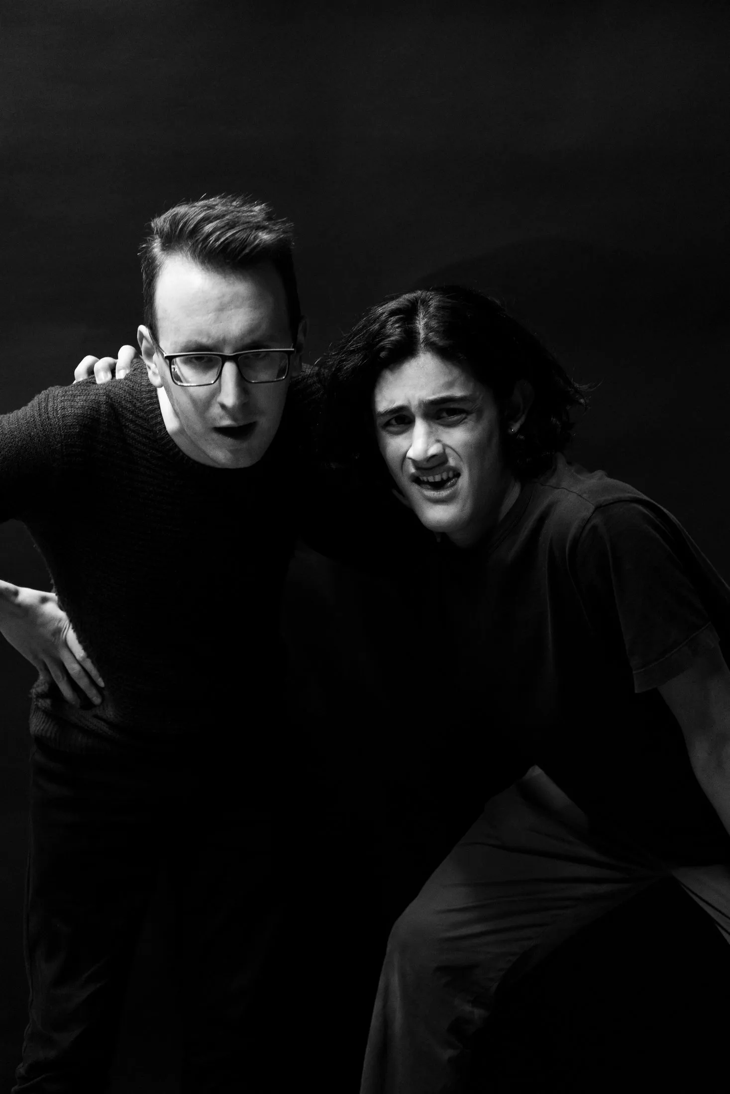 Performers on a dark stage in an Ondine photograph, one seated with a hand raised and another standing.